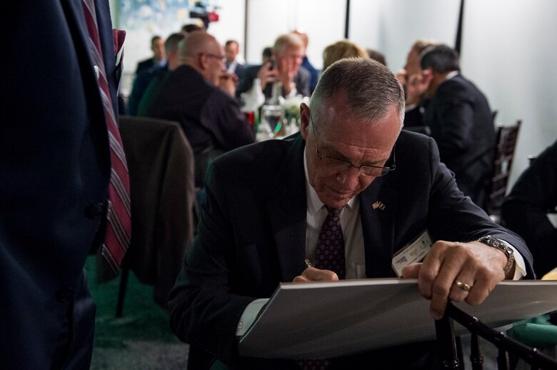 Wayne Fisk, a Jolly Green Association (JGA) member, signs a piece of art during the banquet celebrating the 50th reunion of the JGA, May 4, 2019, in Fort Walton Beach, Fla. The JGA presented Airmen from the 41st Rescue Squadron (RQS) and the 48th RQS with the Rescue Mission of the Year award; the only non Air Force rescue award recognized by the Air Force. (U.S. Air Force Photo by Staff Sgt. Janiqua P. Robinson)