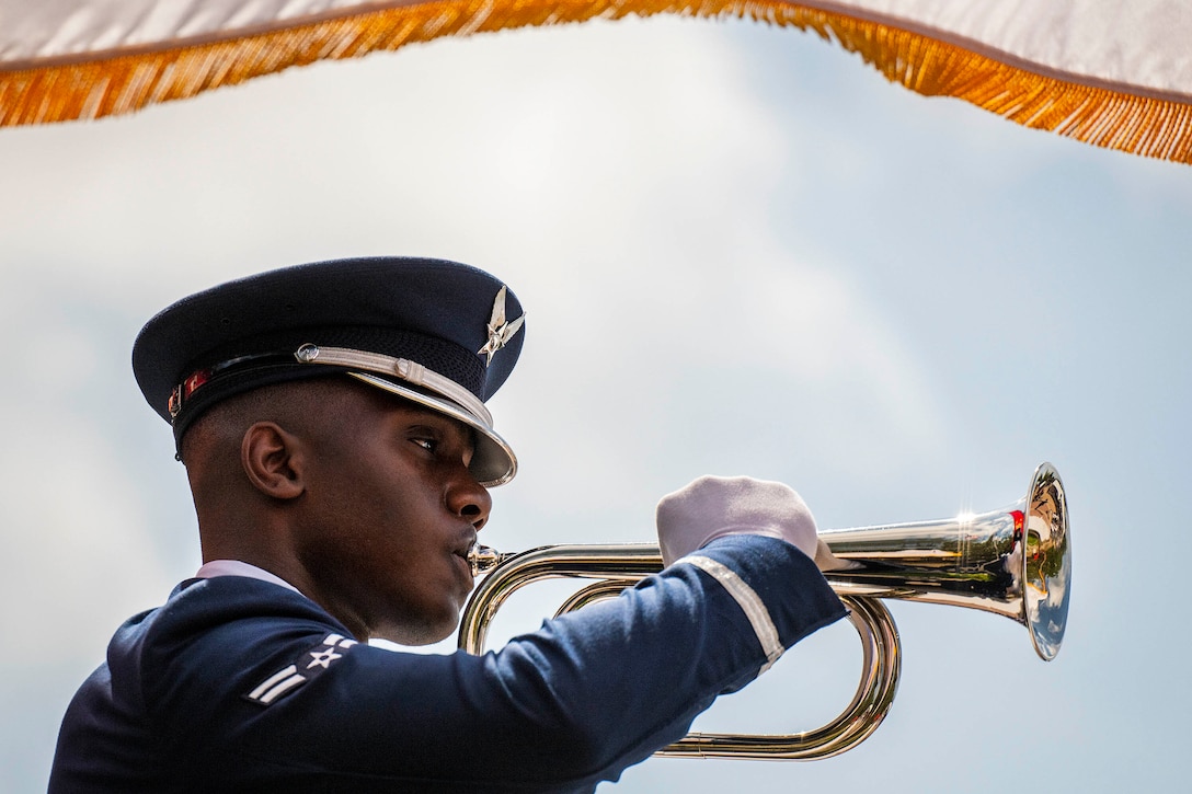 An airman holds a bugle to his lips.