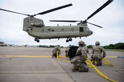 Members of the Downed Aircraft Recovery Team (DART) with Company B, 834th Aviation Support Battalion brace as a UH-47 Chinook helicopter approaches for a sling load operation May 4, 2019 at the Army Aviation Support Facility #2 in Tulsa, Oklahoma. The exercise involves lifting the body of a Chinook helicopter with another Chinook in order to train Soldiers in the recovery of downed aircrafts in combat.