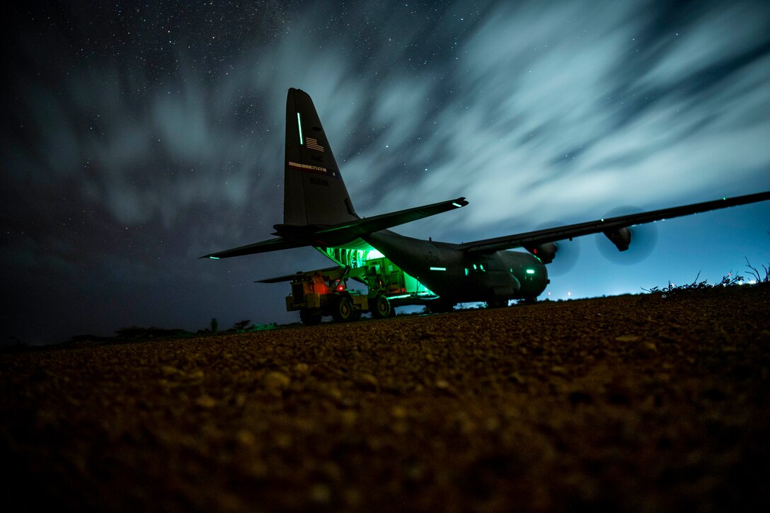 A forklift waits at the back bay of a transport aircraft on a starry night as troops unload cargo.