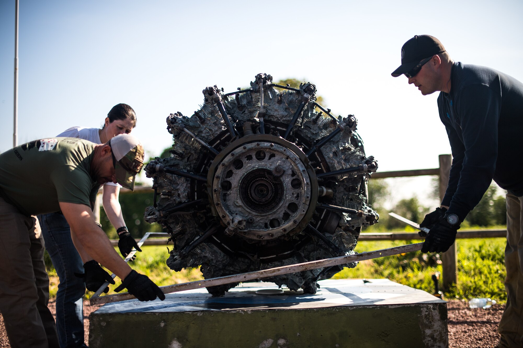 Airmen assigned to the 435th Construction Training Squadron lower a metal frame onto the pedestal of a WWII aircraft display at a memorial in Picauville, France, April 30, 2019. The frame was used to anchor the new display case so the engine could be protected from weather. (U.S. Air Force photo by Staff Sgt. Devin Boyer)
