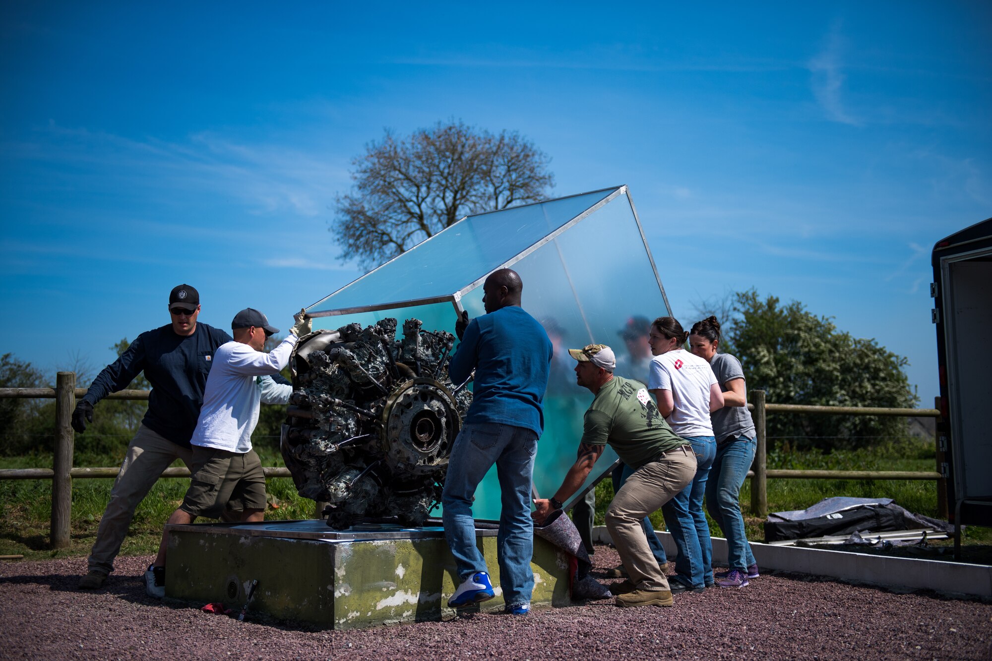 U.S. Air Force Airmen assigned to the 435th Construction Training Squadron and 435th Contingency Response Support Squadron lift a new display case over a WWII aircraft engine at a memorial in Picauville, France, April 30, 2019. The 435th CTS team built the new case from scratch, transported it from Ramstein Air Base, Germany, and mounted it to the pedestal of the display. (U.S. Air Force photo by Staff Sgt. Devin Boyer)
