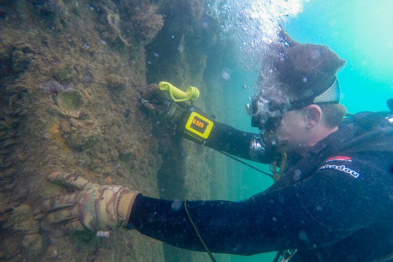 A sailor examines a wharf from underwater.