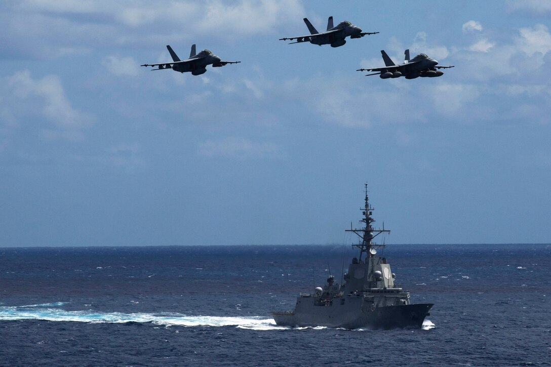 Three planes fly in formation above a ship.