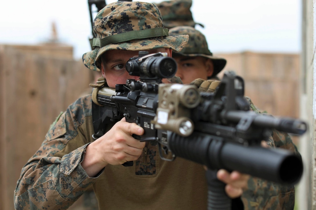 A Marine looks through the scope of his weapon with another Marine in behind.