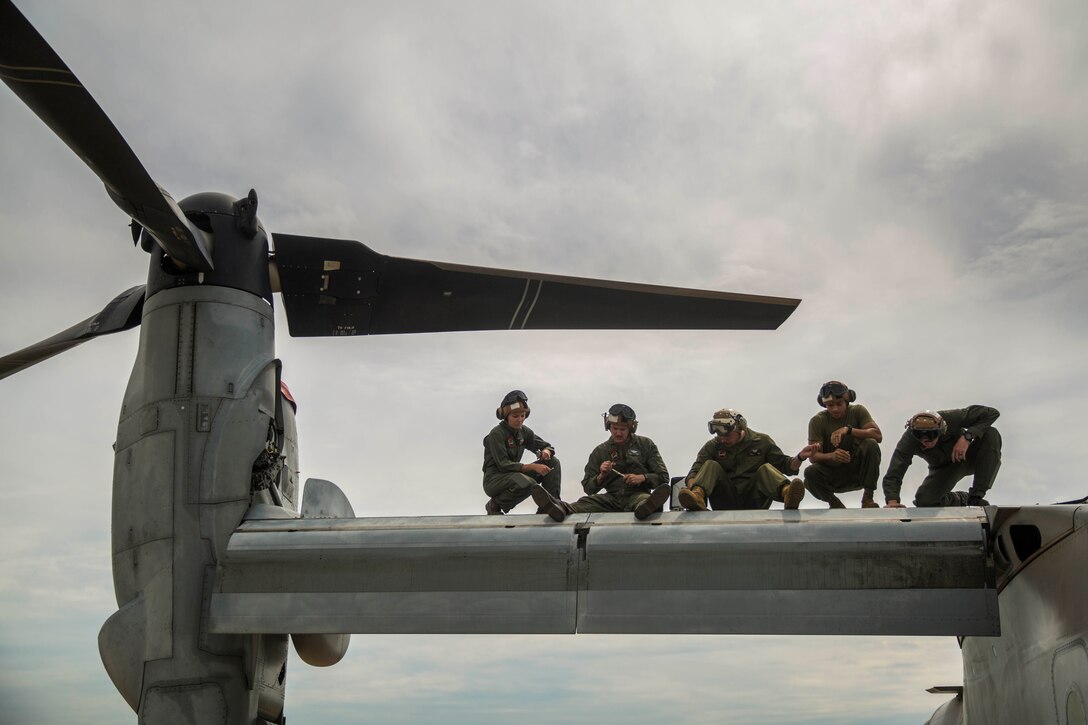 Five Marines sit on the wing of an aircraft.