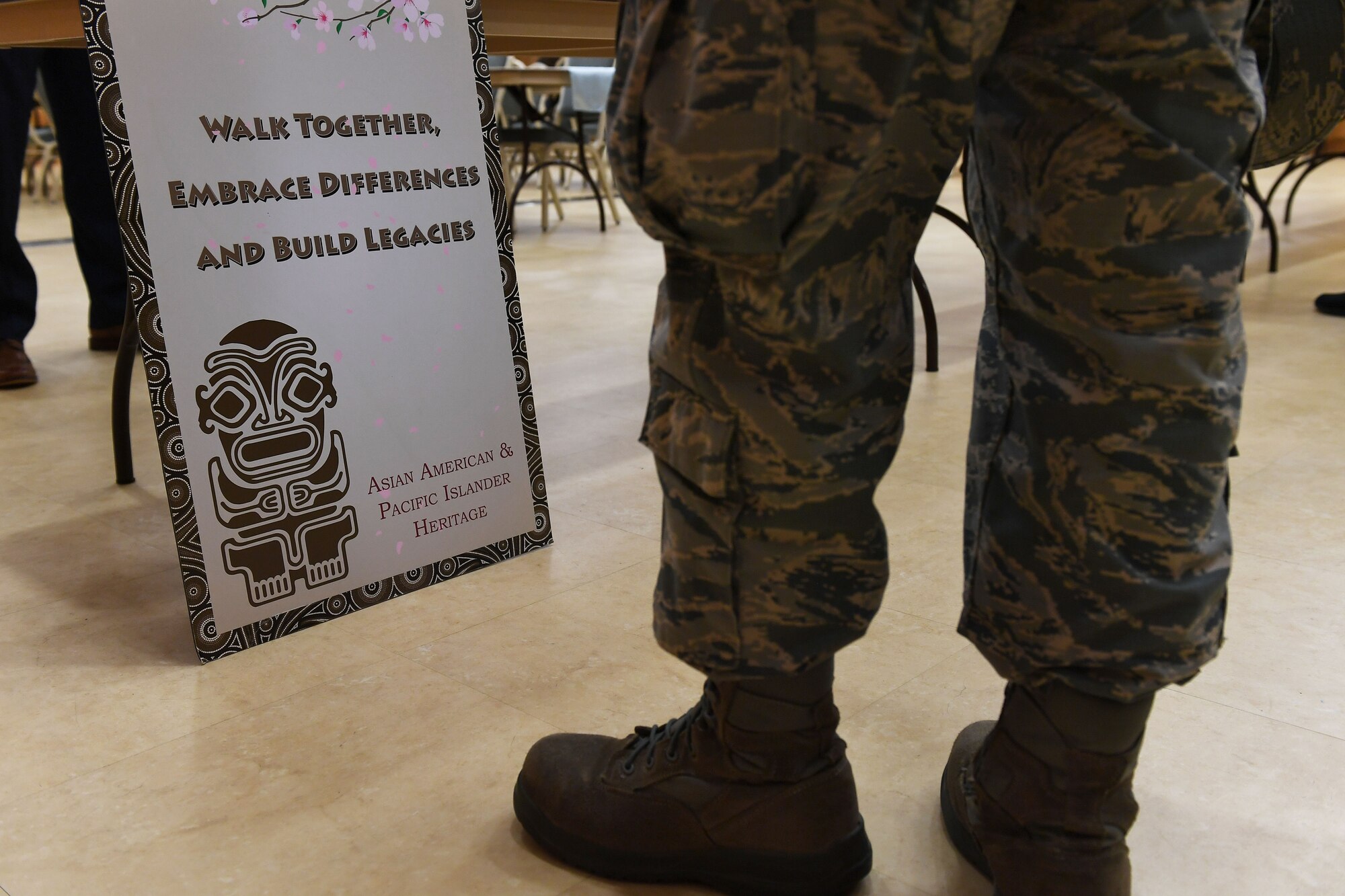 A person's feet stand in front of a sign on the ground and in front of a table.