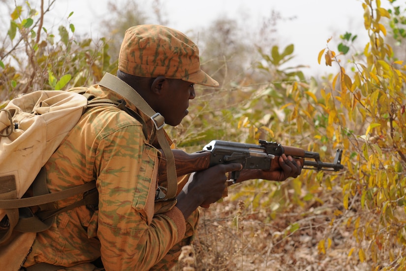 Man with rifle moves through foliage.