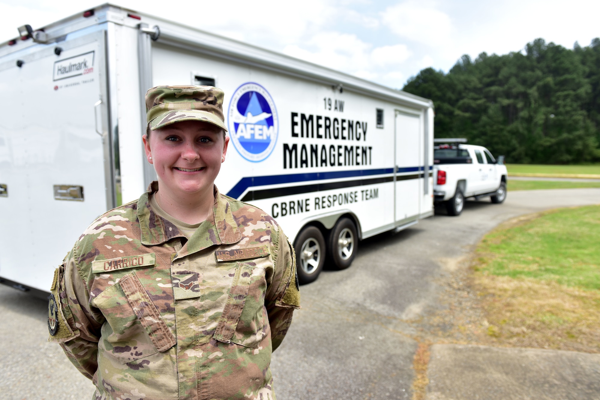 A woman in the operational camouflage pattern uniform stands in front of a truck with the words "Emergency Management" painted on the side.