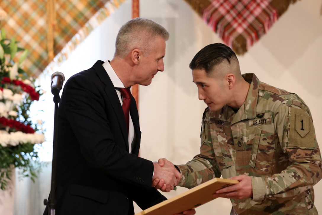 A man in a suit presents award to soldier in uniform.