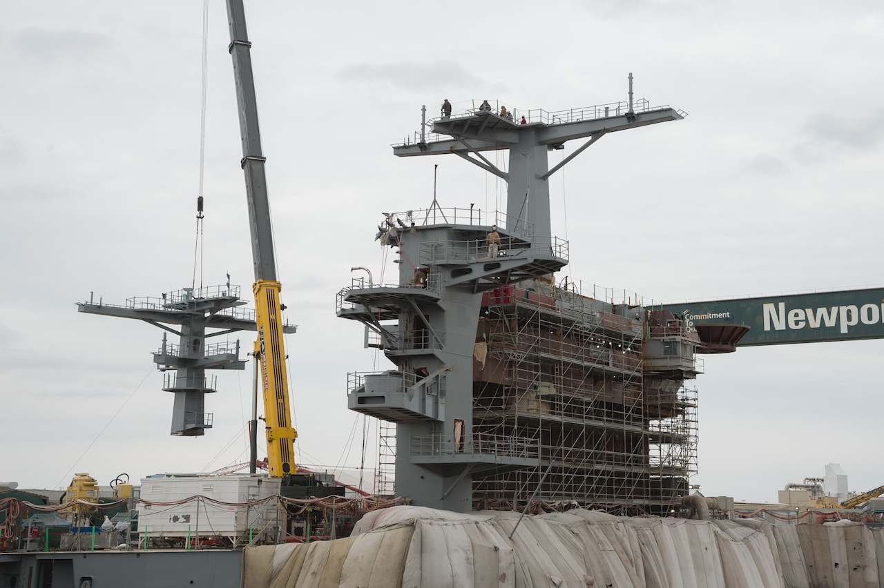 A crane lowers a ship’s mast into place.