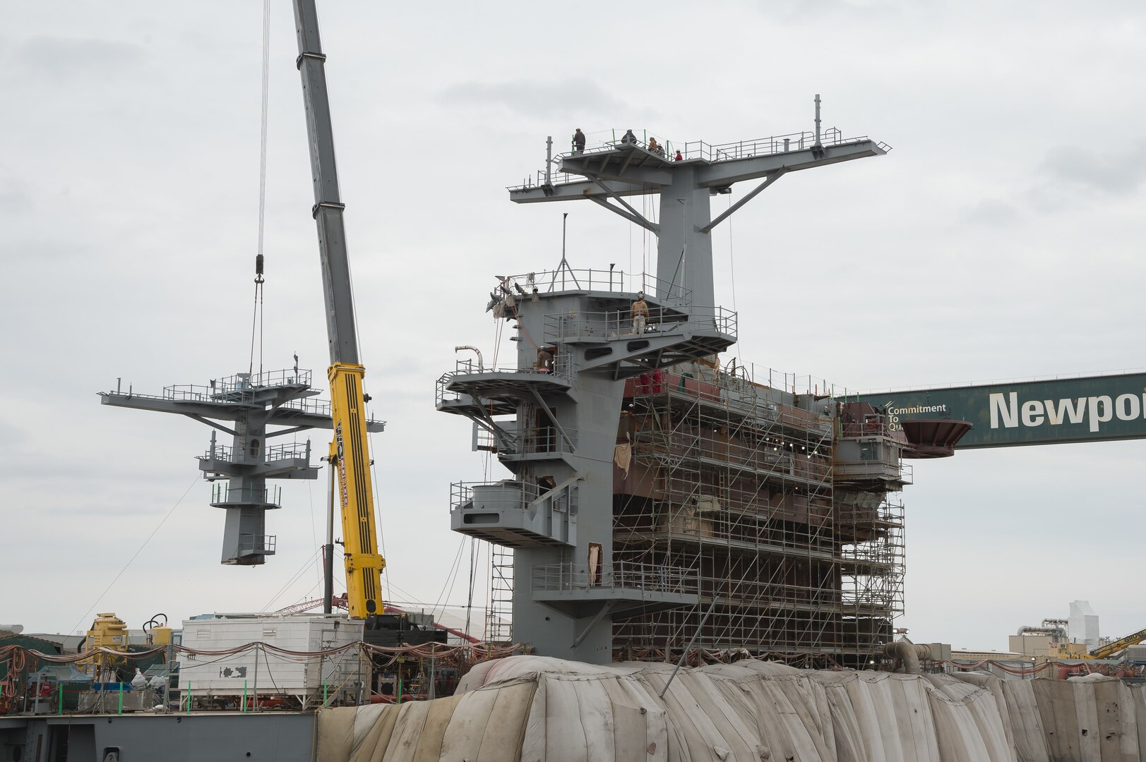 A crane lowers a ship’s mast into place.