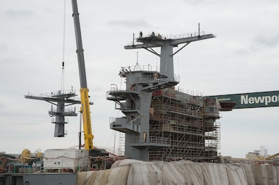 A crane lowers a ship’s mast into place.
