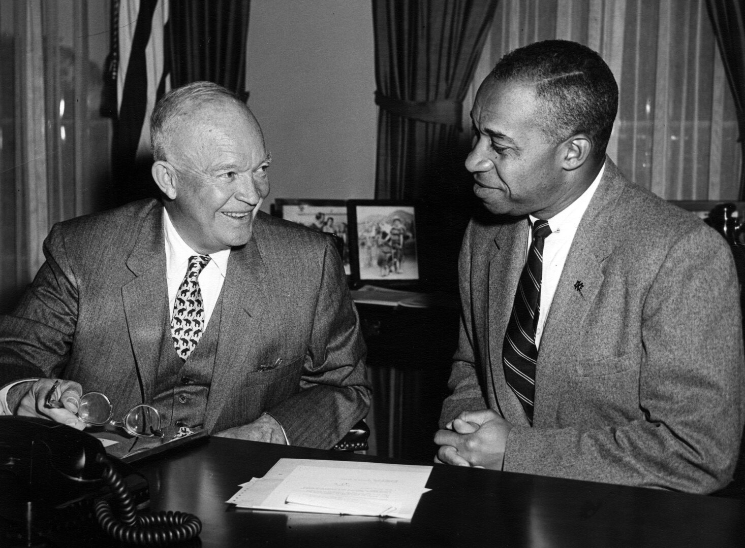 Dwight D. Eisenhower sits at a desk with a member of the White House staff.