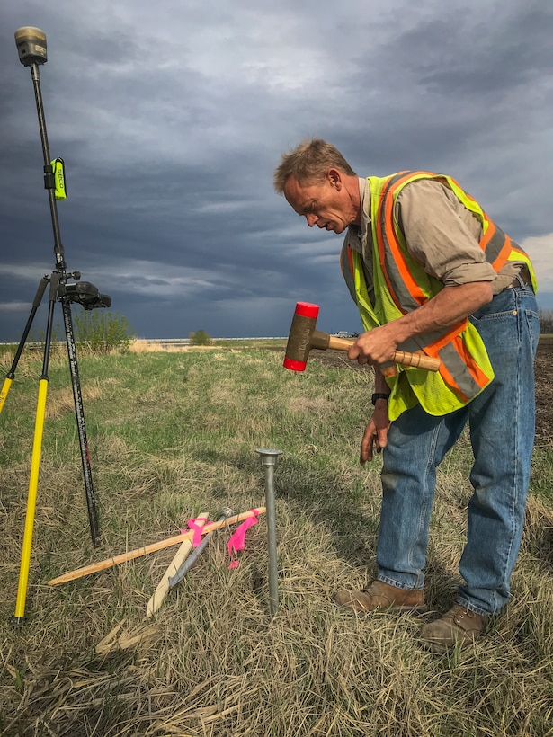 man pounds survey equipment into ground