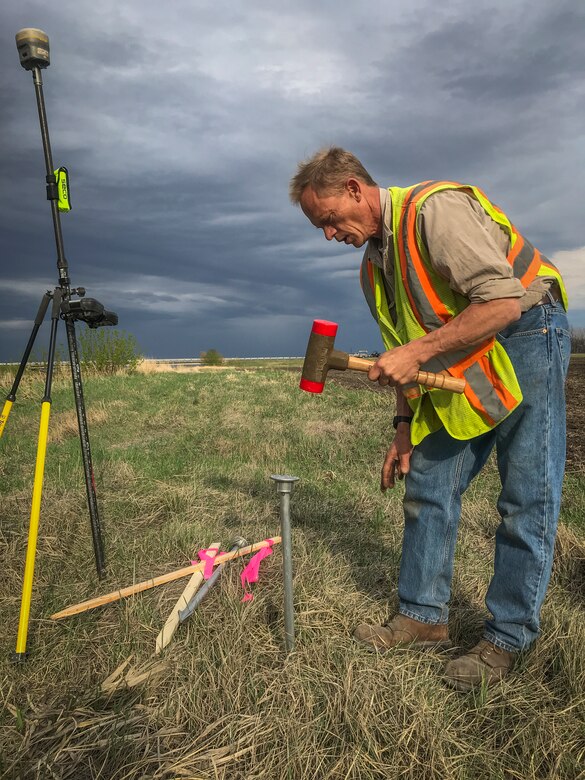 man pounds survey equipment into ground