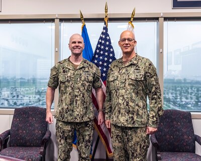 Two military Navy Rear Admirals stand in front of flags