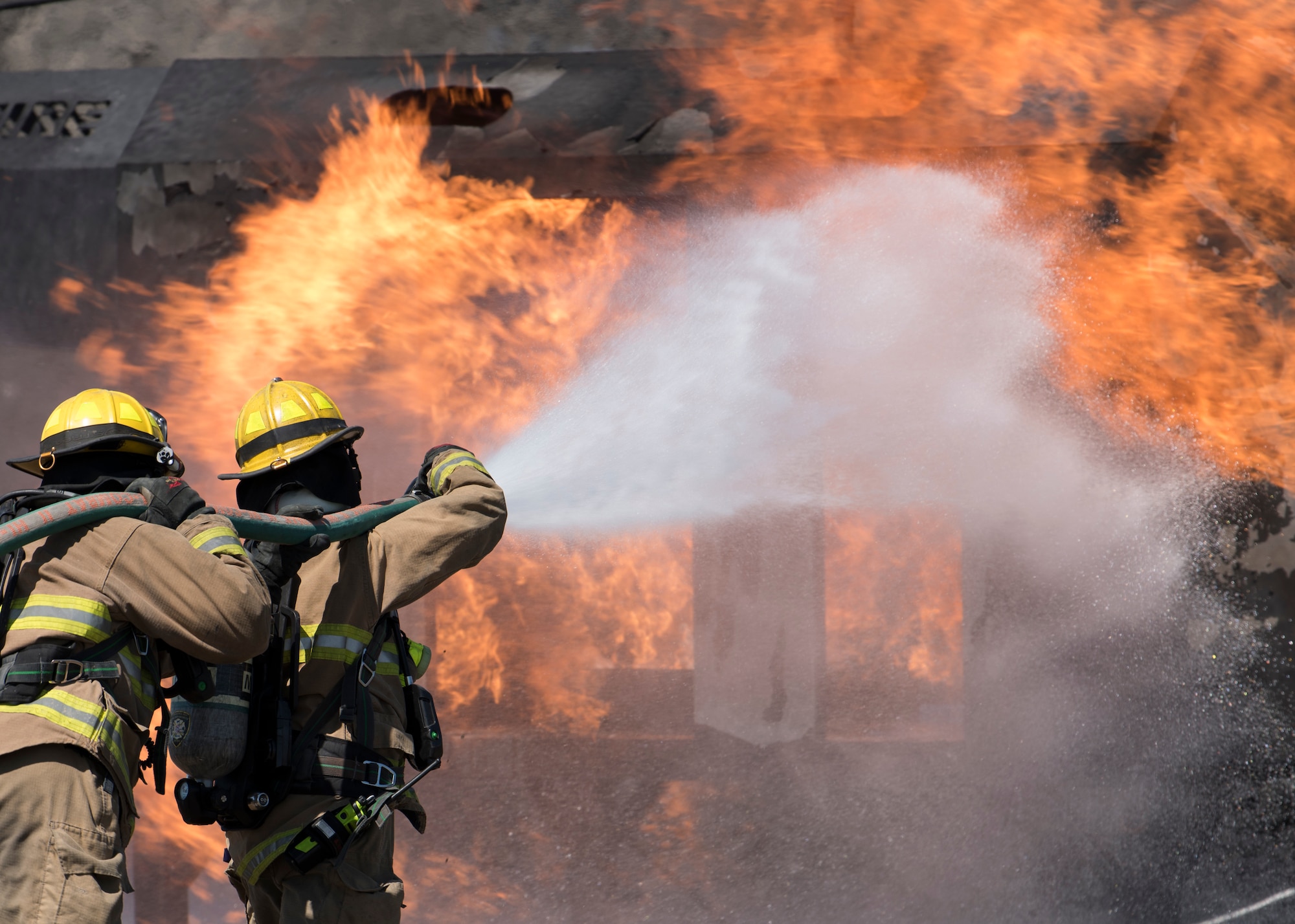 Firefighters from the Airway Heights Fire Department wrestle a hose while approaching a helicopter crash trainer during a Major Accident Response Exercise drill near Fairchild Air Force Base, Washington, May 9, 2019.