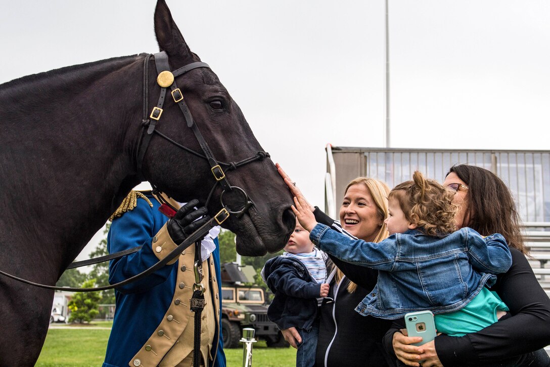 Civilians pet a horse as a soldier holds its reins.