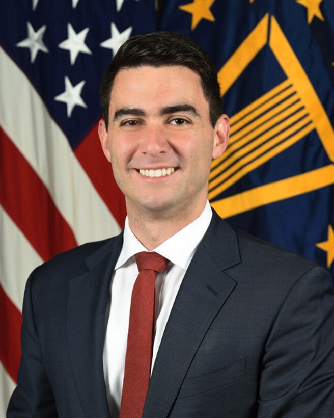 A portrait photo of Matthew Daniels standing in front of the U.S. flag.