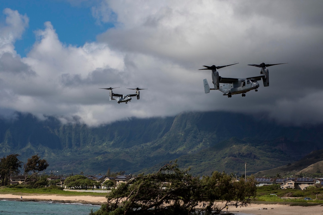 Two military planes fly above a beach in Hawaii.