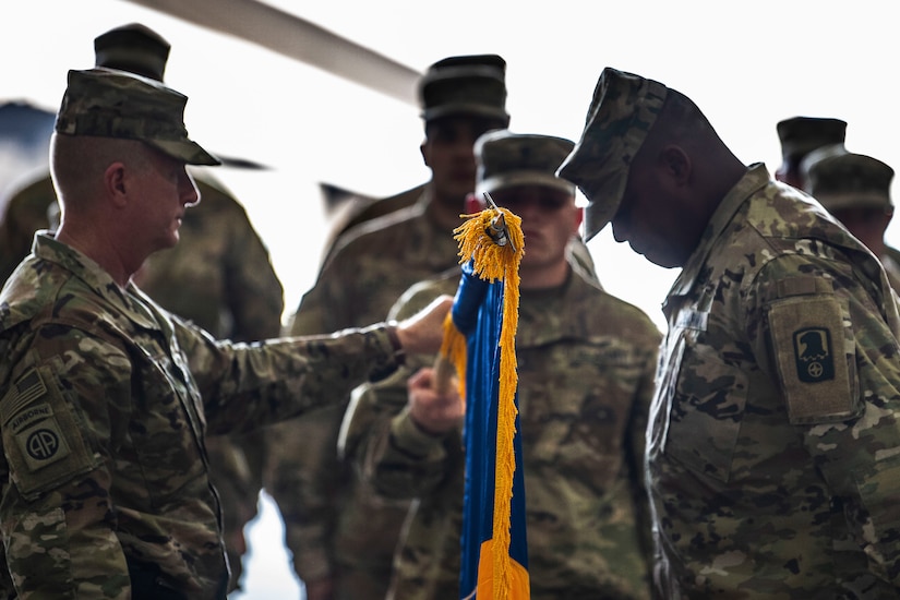 U.S. Army Col. Harvey Cutchin (left), 244th Expeditionary Combat Aviation Brigade, U.S. Army Reserve, and U.S. Army Command Sgt. Maj. Rogelio James, Jr., 244th ECAB (right), unfurl their unit flag during a transfer of authority ceremony in an aircraft hangar in Taji, Iraq, May 1, 2019.  The 244th ECAB supports Combined Joint Task Force – Operation Inherent Resolve and Operation Spartan Shield.  CJTF-OIR works with partner forces to defeat Daesh in designated areas and set conditions for follow-on operations to increase regional stability.