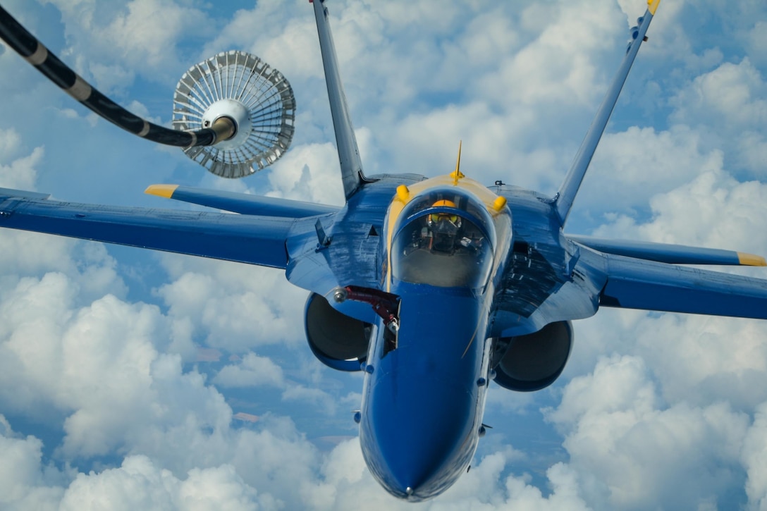 A blue military jet flies above the clouds as it prepares to get refueled.