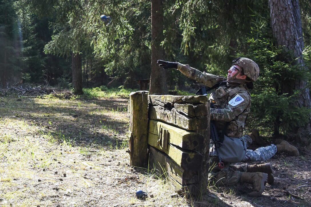 A soldier throws a training grenade from behind a wooden barrier.