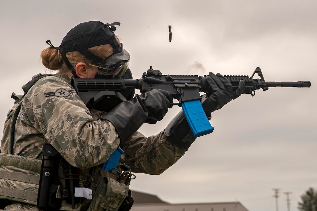 An airman wearing a gas mask fires a weapon.