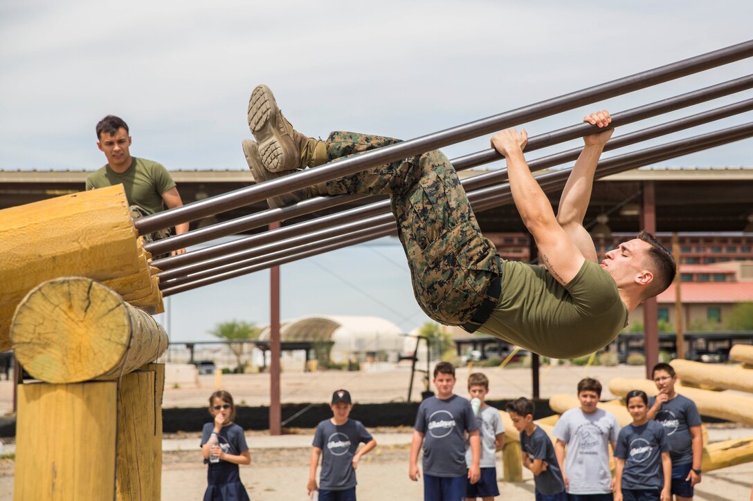 A Marine slides down a pole upside down while a group of young children watch.