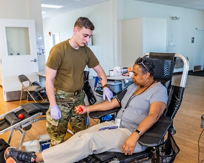 Military man touches vein on sitting woman in preparation of giving blood