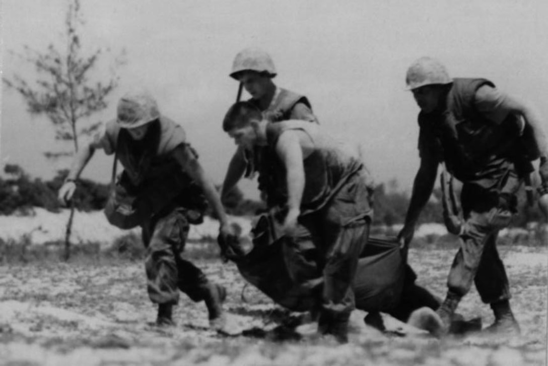 Four Marines on a battlefield carry an injured Marine on a makeshift gurney.