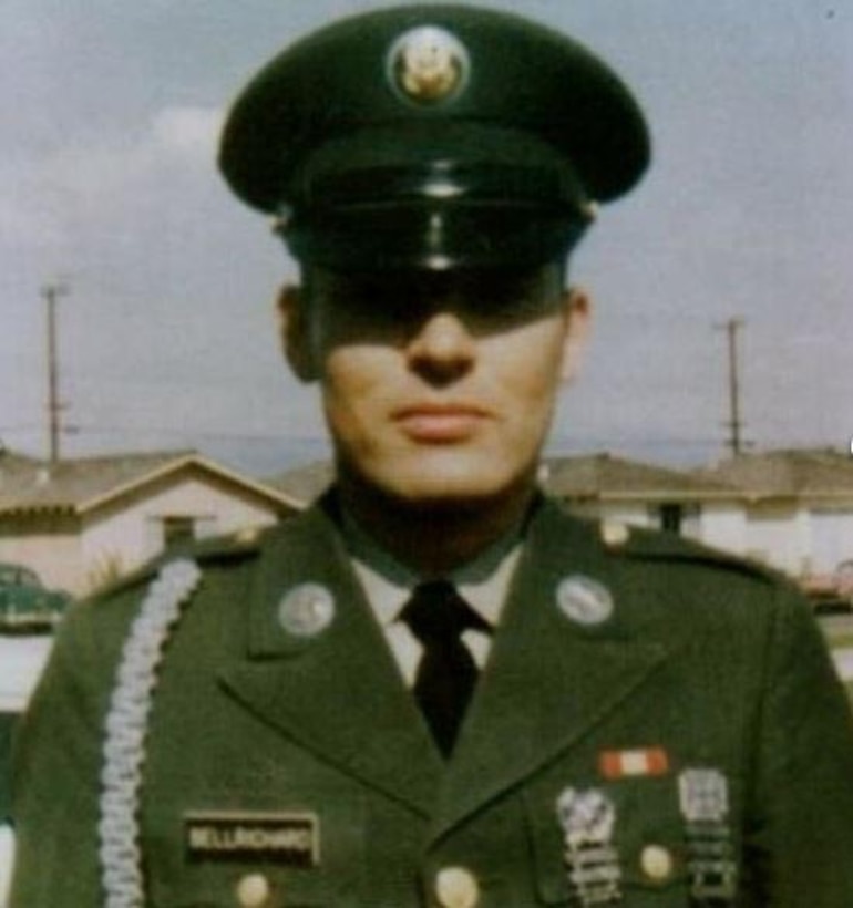 A soldier in dress uniform stands at attention wearing a formal cap.