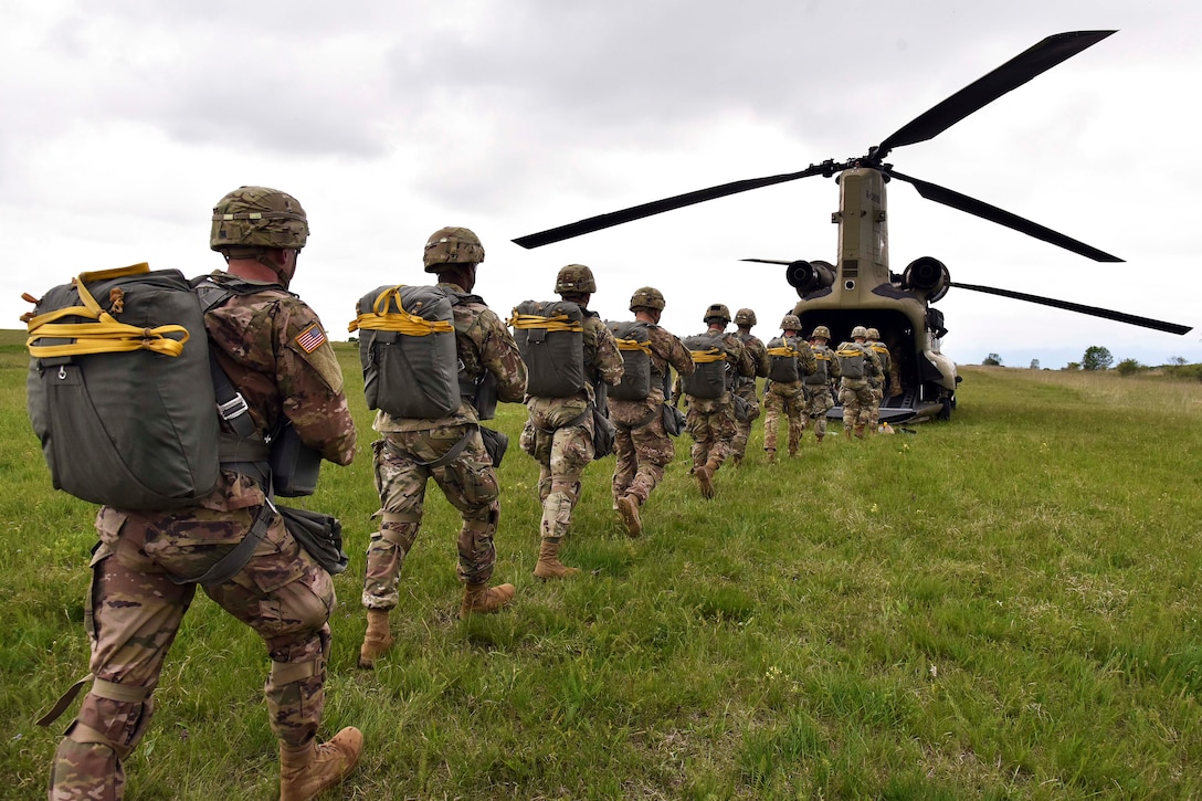 Soldiers walk in a single line as they enter a helicopter.