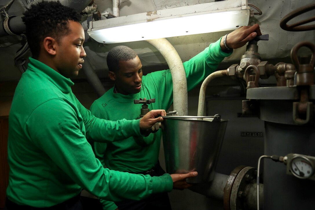 Two Seamen vent a  hydraulic filter below deck.