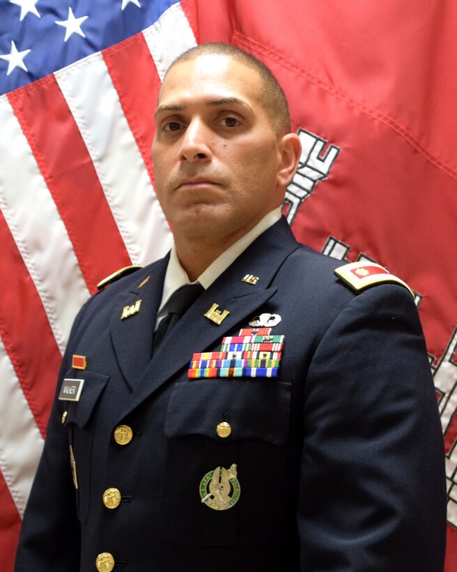 Maj. Alexander Walker wearing Army Service Uniform in front of USA and USACE flags.
