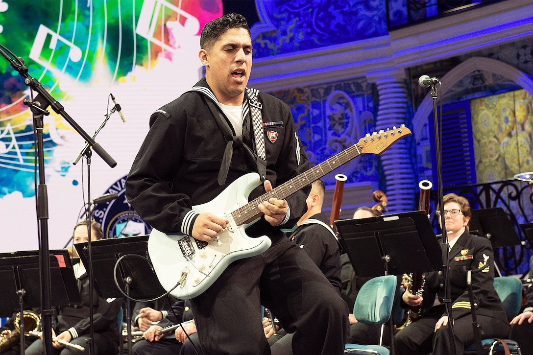 A sailor plays the guitar on stage during a concert.