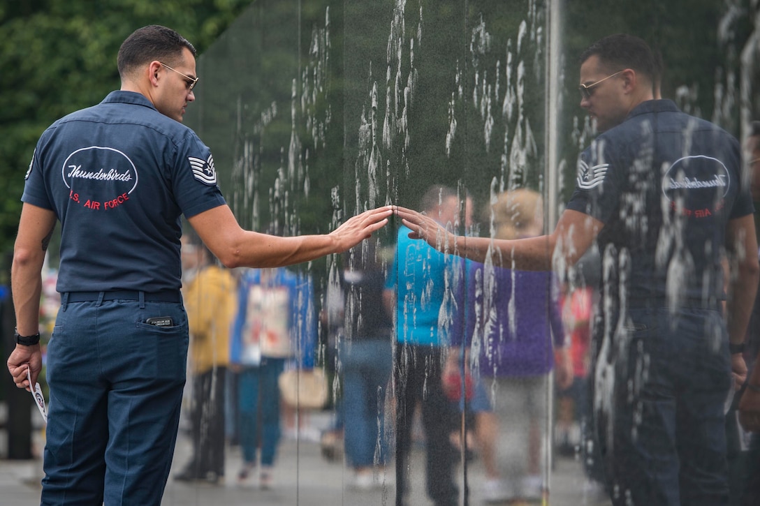 A man looks at his reflection in the wall of a memorial.