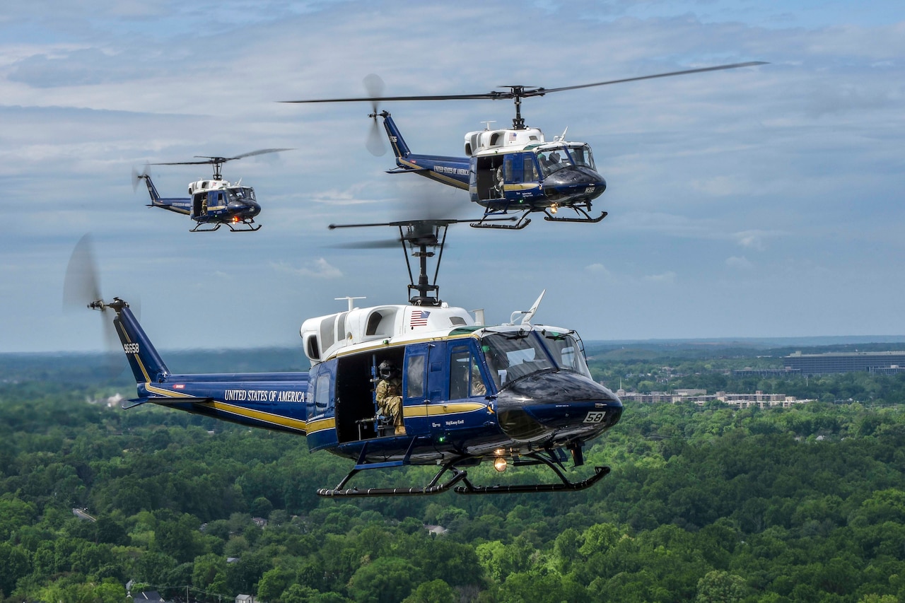 Three military helicopters fly above trees.