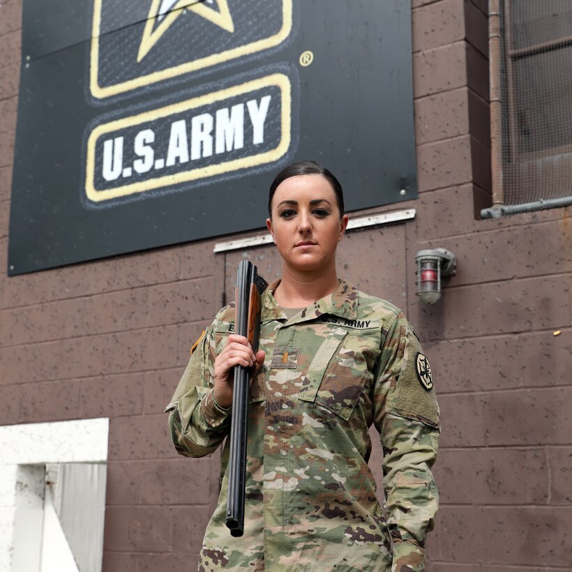 Female soldier in camouflage uniform poses with her shotgun.