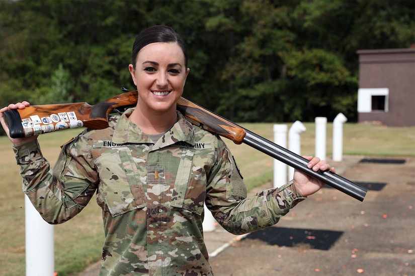 Female soldier in camouflage uniform poses with her shotgun on her back.