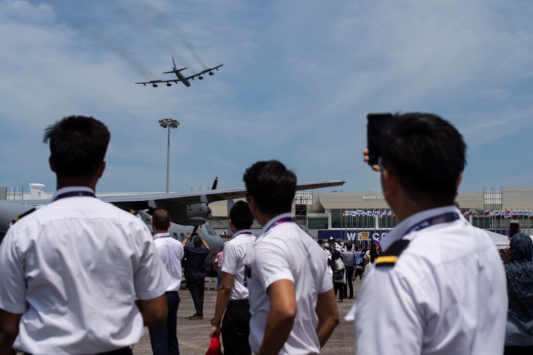 A bomber flies over a crowd of uniformed personnel.