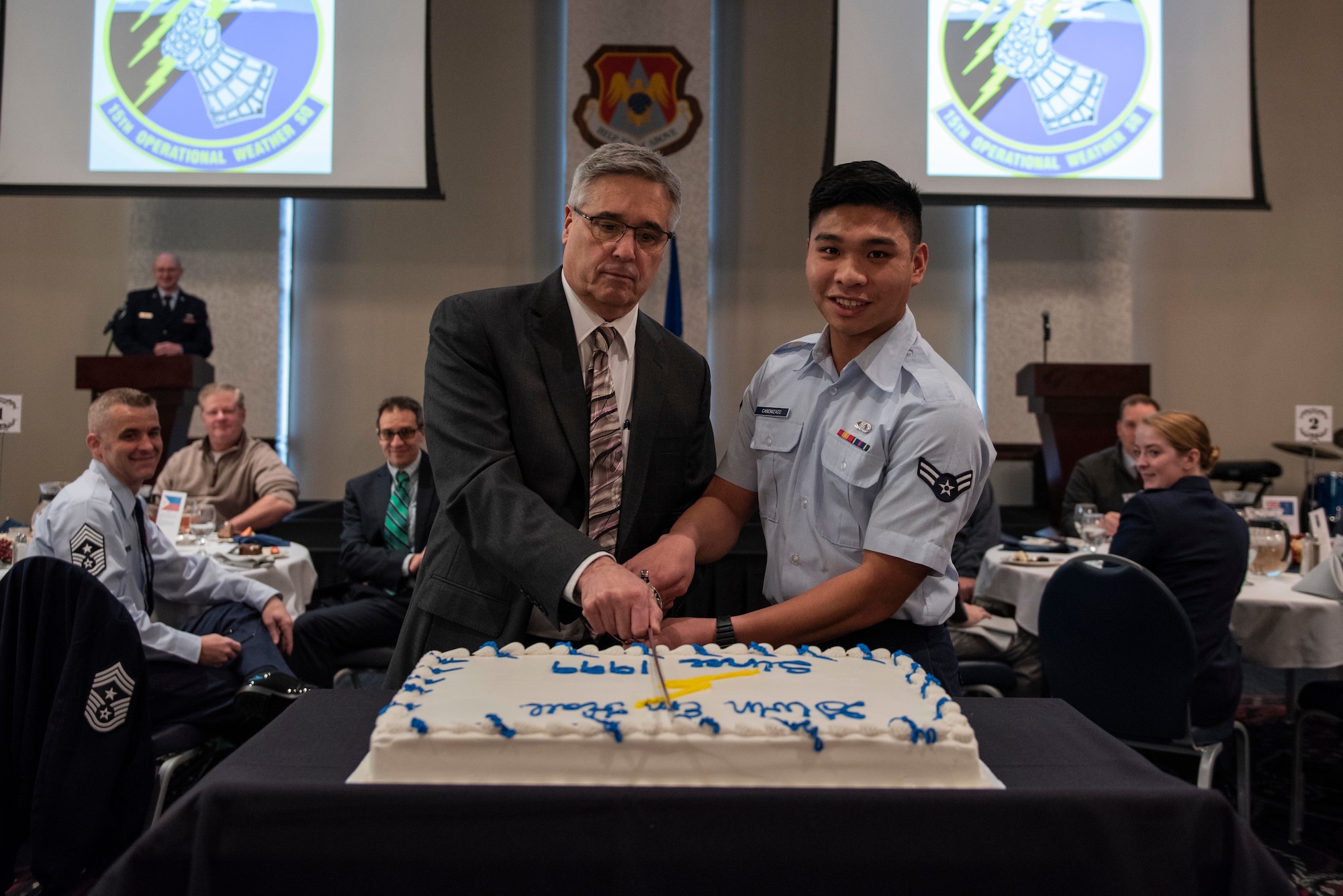 Frederick Wirsing, Air Mobility Command chief weather operations and plans branch, and U.S. Air Force Airman 1st Class Arjay Canonizado, 15th Operational Weather Squadron forecaster, cut the cake at the 15th OWS 20th anniversary dinner, Feb. 12, 2019, at Scott Air Force Base, Ill. During its 77 years, the 15th OWS has been located in six states and four countries across three different continents. It has spent the last 20 years assigned to Scott. (U.S. Air Force photo by Senior Airman Daniel Garcia)