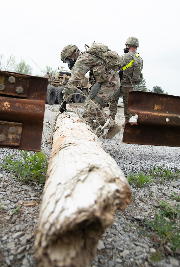 U.S. Soldiers with the 62nd Engineers, 104th Engineer Construction Company, from Ft. Hood, Tx., wrap a chain around a downed utility pole in preparation for the Heavy Expanded Mobility Tactical Truck (HEMTT) to pull it from a road at Muscatatuck Urban Training Center in Butlerville, Indiana, during Guardian Response 19, a homeland emergency response exercise which tests the ability of the military to respond to a man-made or natural disaster on April 30, 2019. The Soldiers are responding to a city following a mock nuclear detonation, so they must don gas masks and protective equipment while working. (U.S. Army photo by Master Sgt. Brad Staggs/released)
