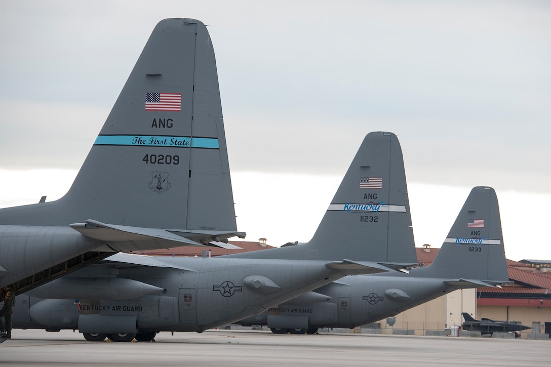 Tails of three C-130 cargo aircraft on a flight line.