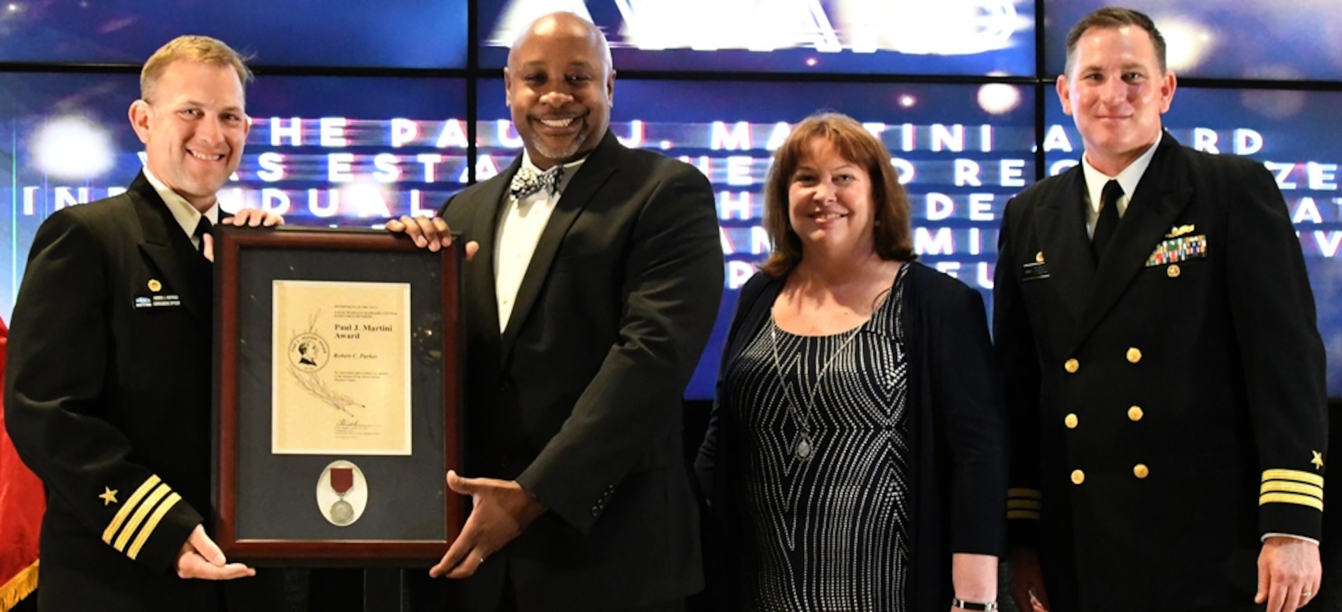 IMAGE: FREDERICKSBURG, Va. (May 10, 2019) – Robert Parker holds the Paul J. Martini Award moments after receiving it from Naval Surface Warfare Center Dahlgren Division (NSWCDD) leadership at the command’s annual honor awards ceremony. Parker was recognized for providing flawless executive assistance to the NSWCDD Dam Neck Activity commanding officer. Standing left to right: NSWCDD Dam Neck Activity Commanding Officer Cmdr. Andrew Hoffman; Parker; NSWCDD Deputy Technical Director Angela Beach; and NSWCDD Commanding Officer Cmdr. Stephen ‘Casey’ Plew.  (U.S. Navy photo/Released)
