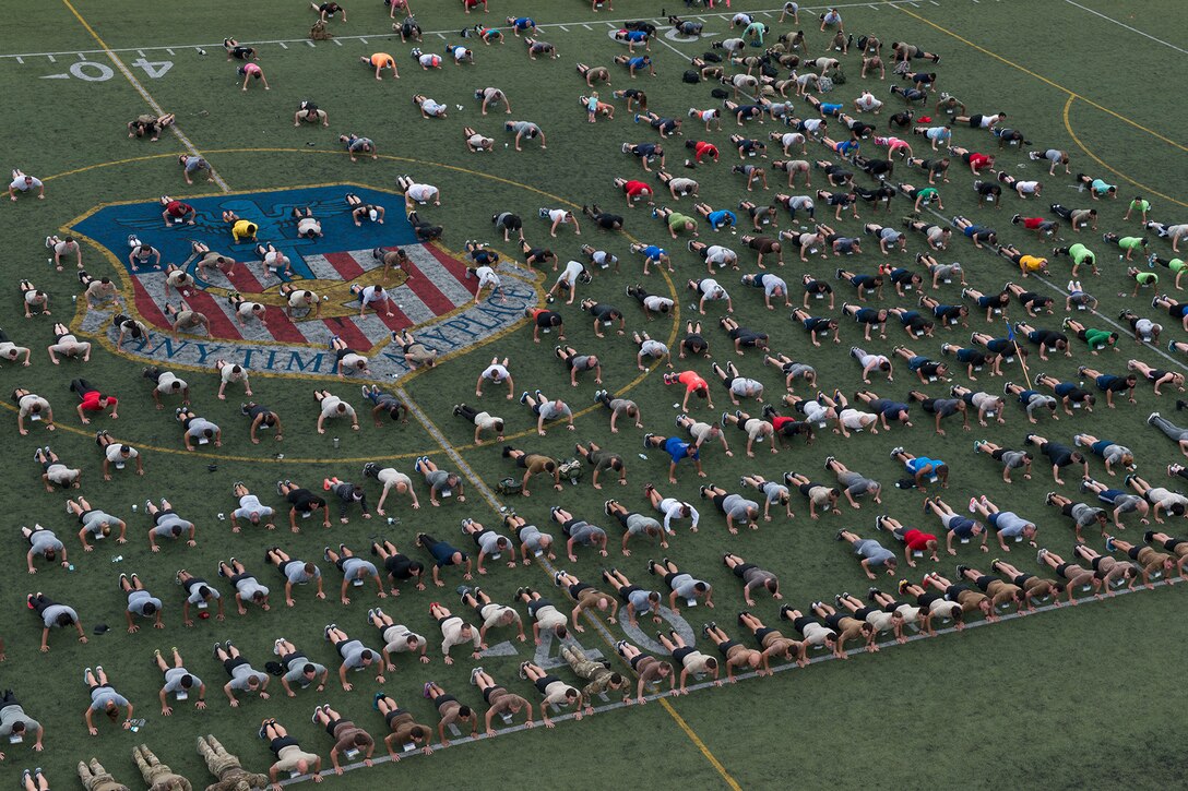 Participants perform pushups in a field during a run.
