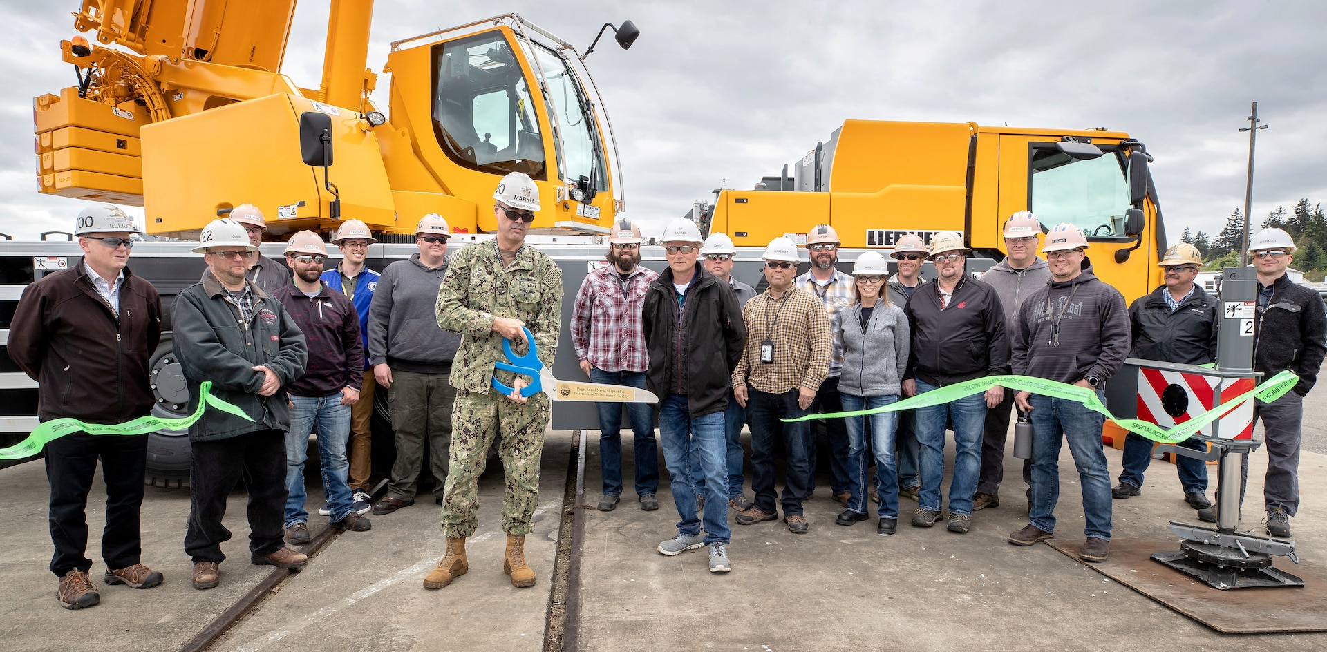 Lifting and Handling Department teammates watch as Capt. Howard Markle, Puget Sound Naval Shipyard & Intermediate Maintenance Facility commander, cuts the ribbon to ceremoniously bring into service the first of four mobile cranes purchased through Naval Sea Systems Command’s Capital Investment Program.