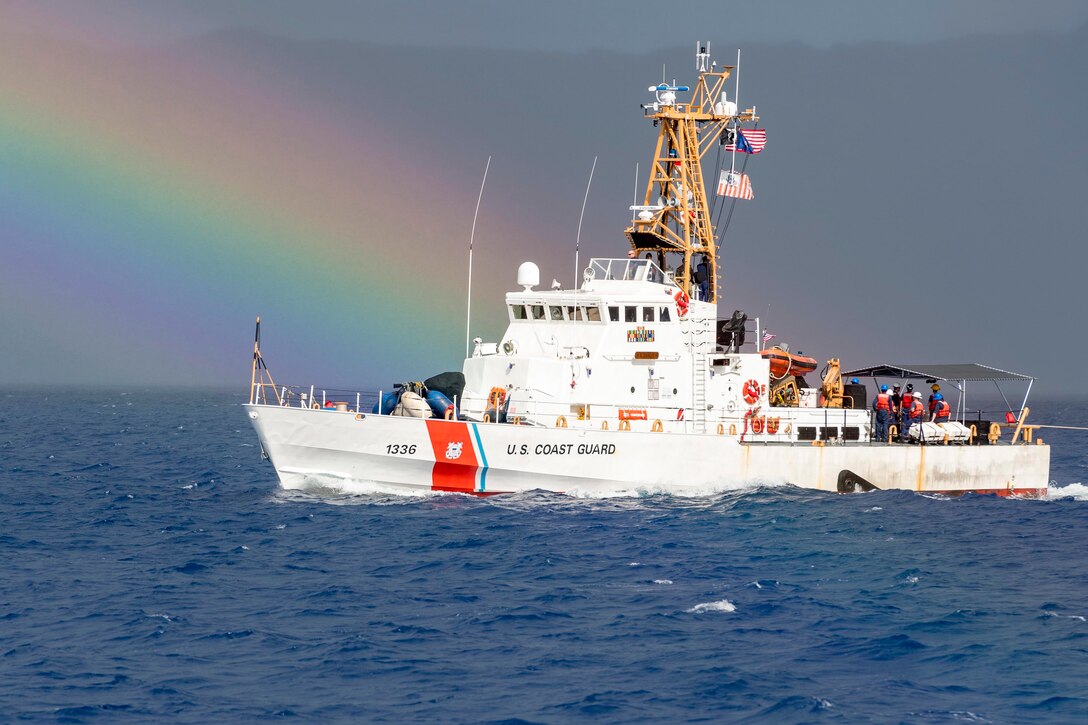 A boat floats on the water with a rainbow across the sky behind it.