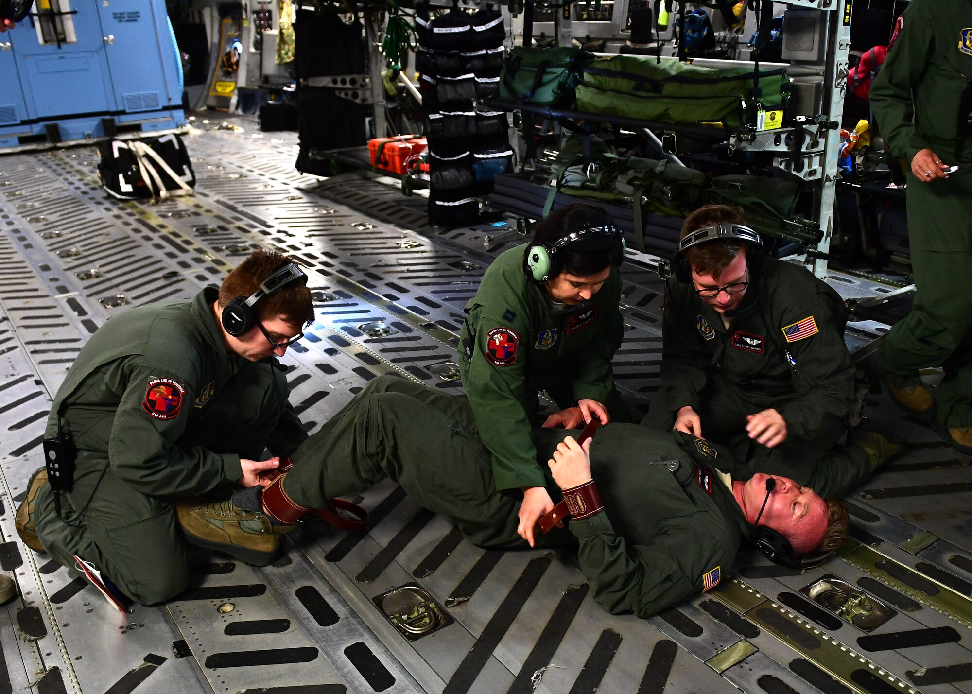 Staff Sgts. Raymond Johnson, John Klobushnik, and Scott Wardo, medical technicians with the 914th Aeromedical Evacuation Squadron, and Capt. Megan Taggert, 914th AES flight nurse, practice putting restraints on a mental health patient above Honolulu, Hawaii April 24, 2019. Johnson was playing the part of the mental health patient while Klobushnik, Wardo and Taggert practiced the restraint procedures. (U.S. Air Force photo by Senior Airman Grace Thomson)